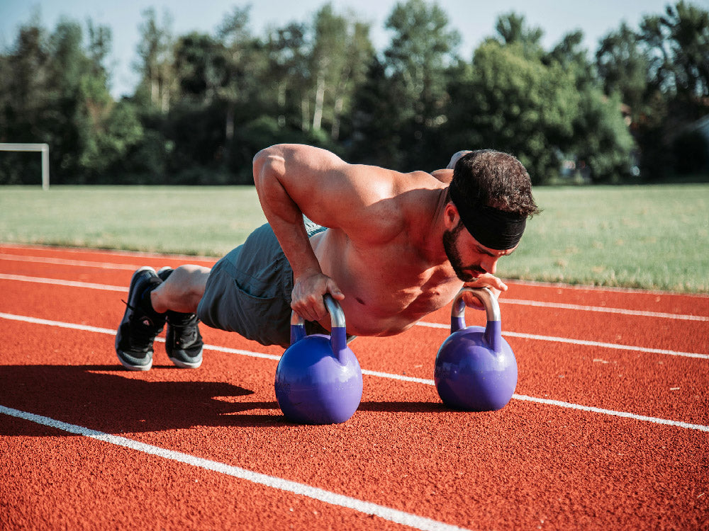 Man doing push ups with kettlebell on running track