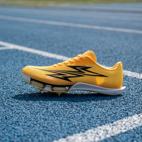A yellow track and field shoe with black graphic accents and a white sole, photographed on a blue running track with white lane lines.