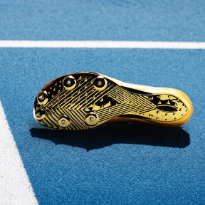 A close-up of a gold track cleat sole with black studs and tread patterns, resting on a blue running track with white lines.