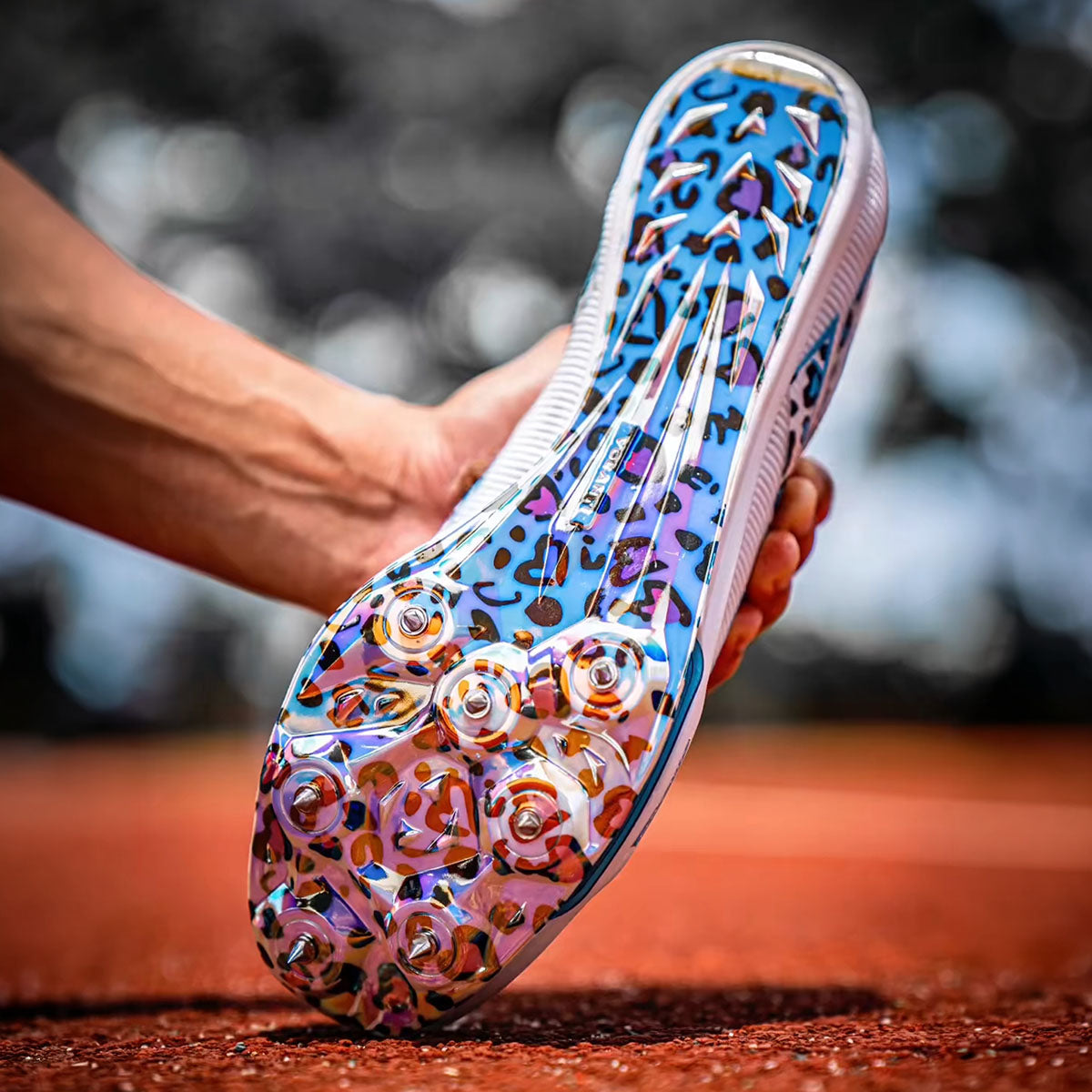 Track spikes with colorful leopard print pattern held by a person against a blurred background