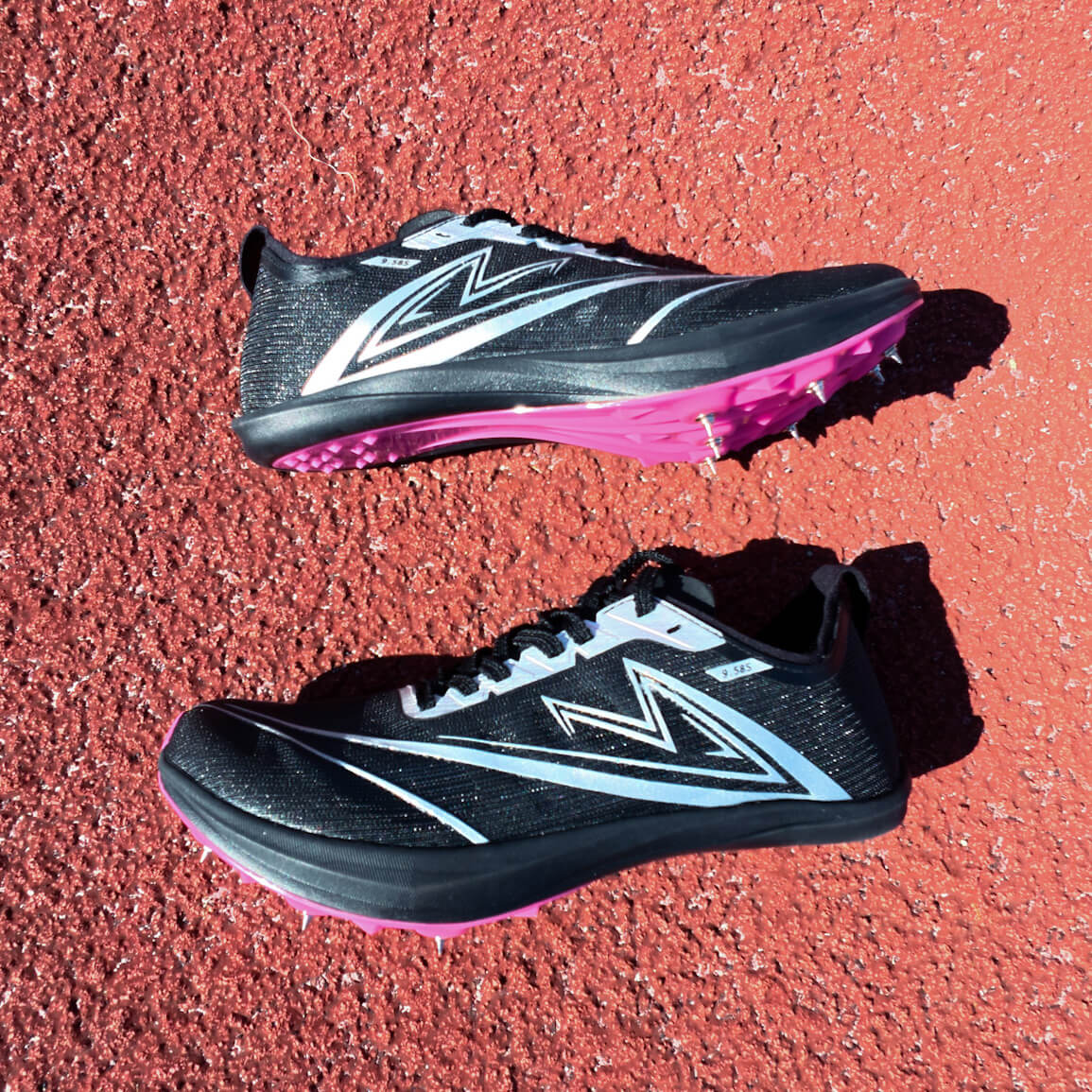 Pair of black and pink running shoes on a red track surface