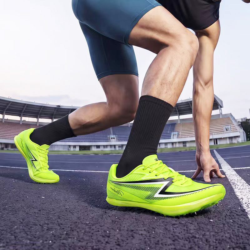 A close-up action shot of a sprinter on a track wearing bright neon yellow-green running shoes with black socks and dark blue track shorts, with stadium stands blurred in the background.